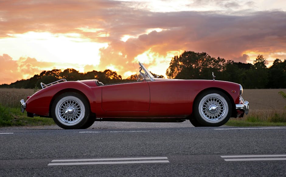 Vintage red convertible car parked on a country road at sunset with dramatic skies