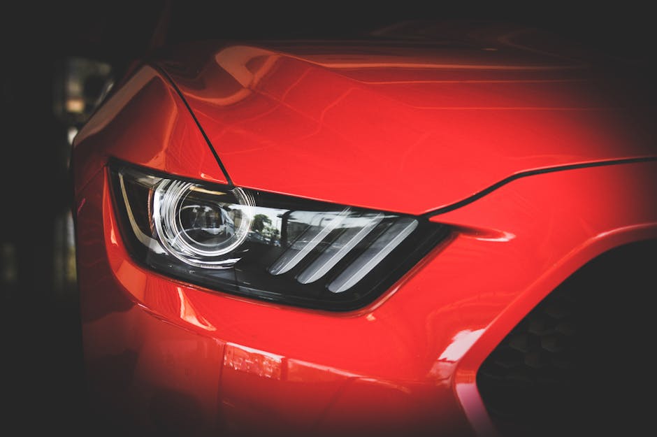 Detailed view of a red Ford Mustang's headlight showcasing sleek automotive design